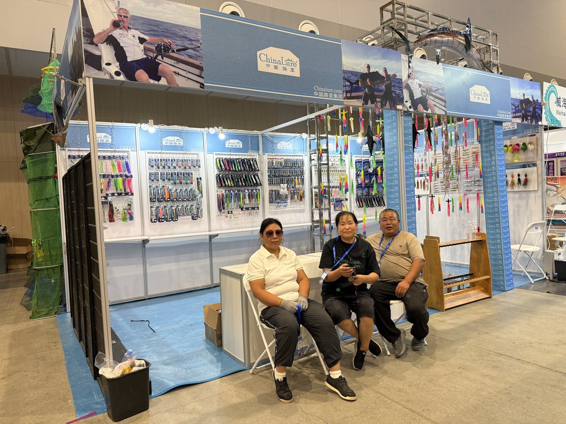 Chinalure booth at the Weihai fishing tackle expo, with walls of lures, rods and rigs and three staff sitting in front
